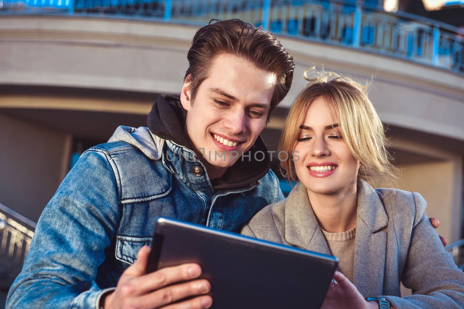 Attractive young couple sitting on floor in urban street reading information on a tablet with a smile