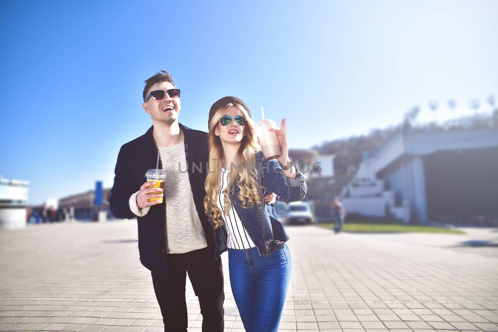 Smiling couple walk at the street in weekend and drink some cocktails.