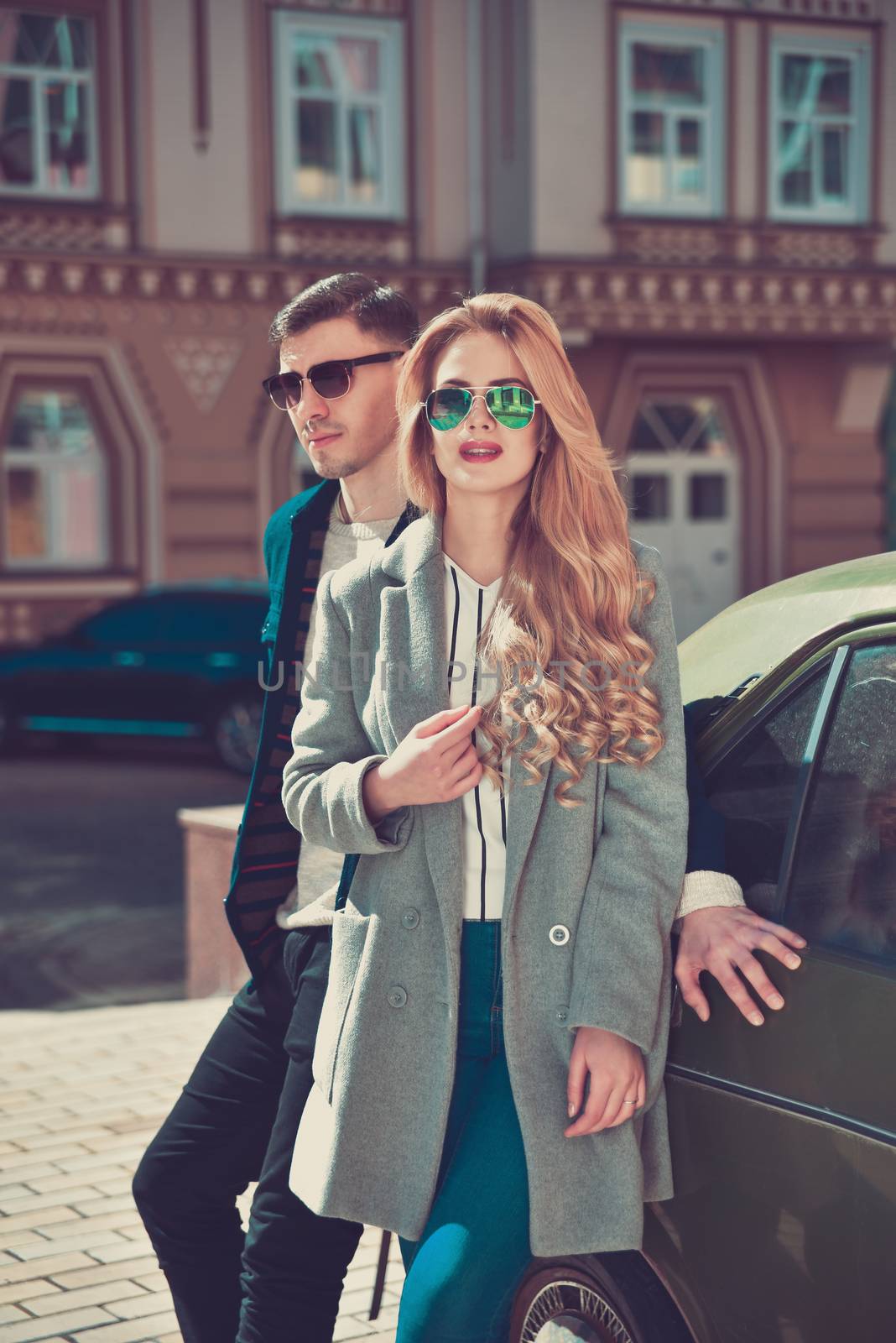 Fashionable couple in sunglasses stand at street near the car