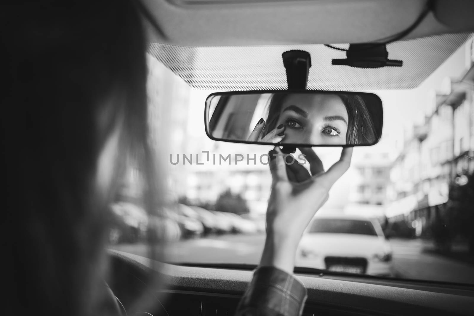 the girl behind the wheel looks in the rear-view mirror in the car and makes herself a make-up in black and white by Nickstock