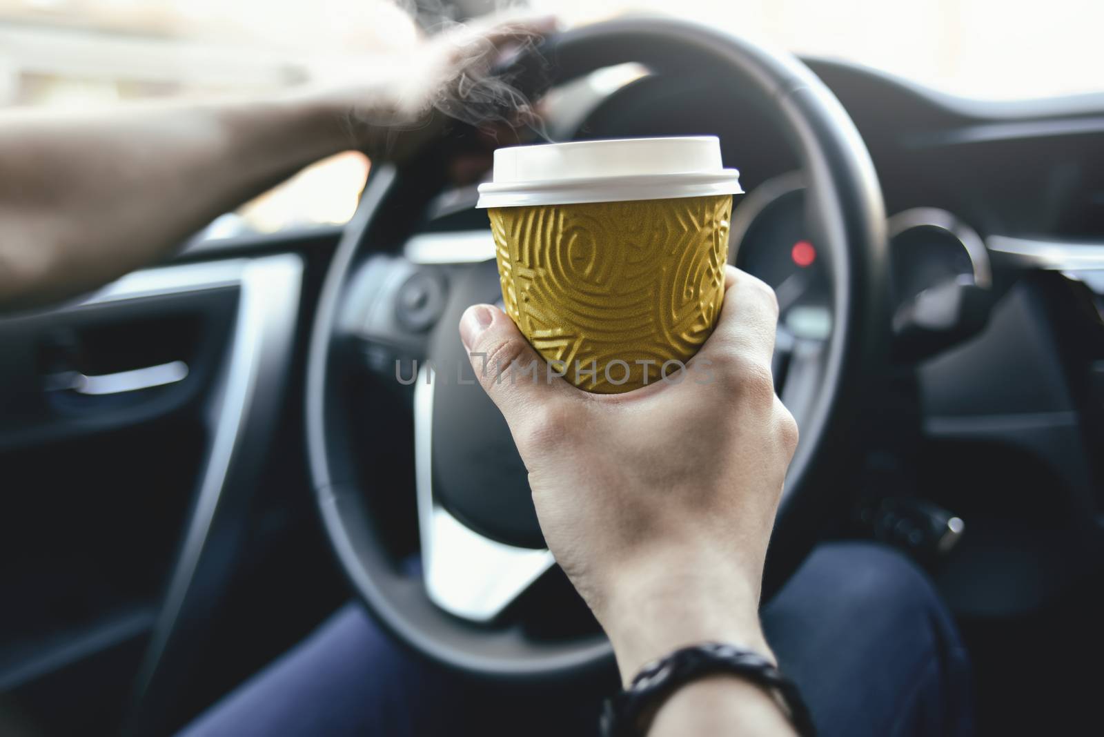 Man arms hold a coffee and rudder in automobile