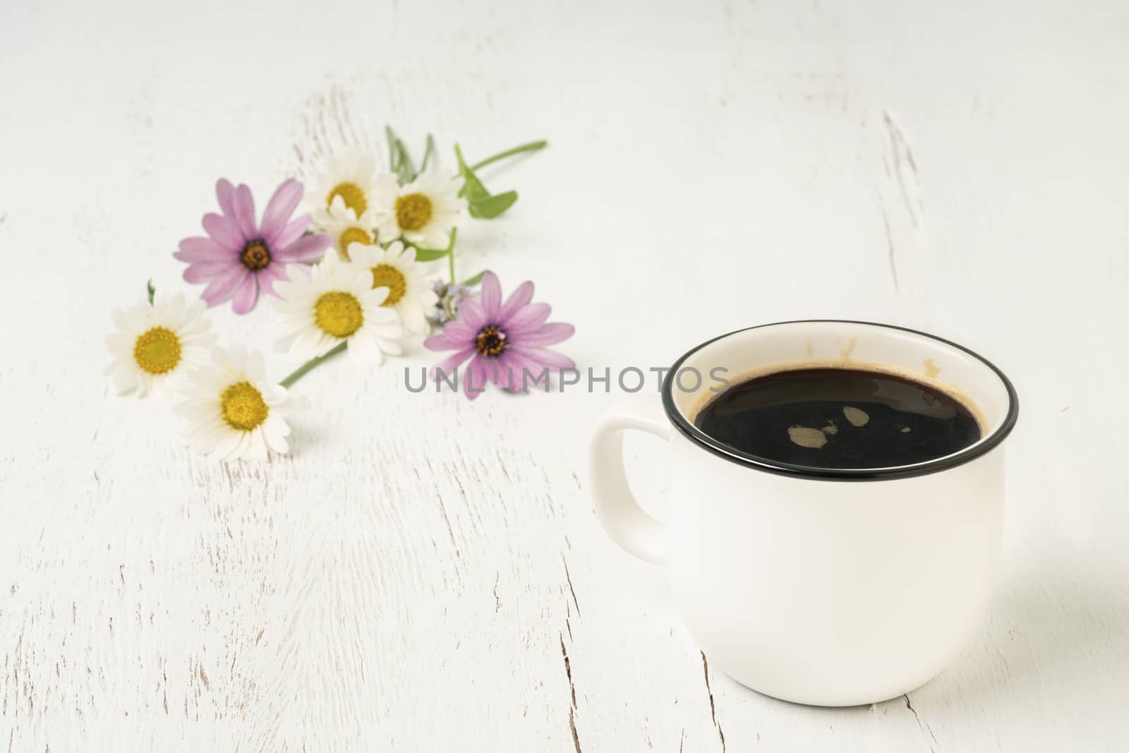 A cup of Americano coffee on a wooden table decorated with spring flowers