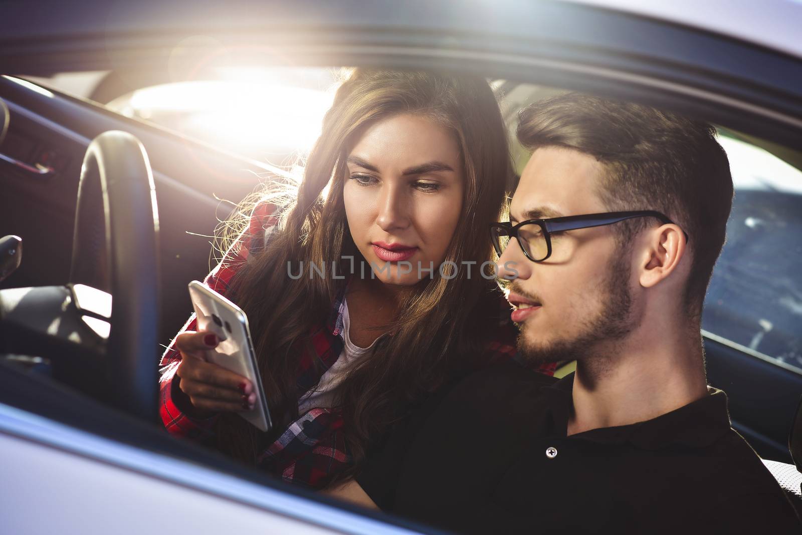 Enjoying travel. Beautiful young couple sitting on the front passenger seats and smiling while handsome man driving a car and use a mobile phone