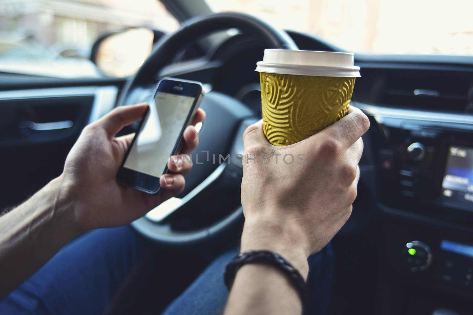 Man arms hold a coffee and phone in automobile