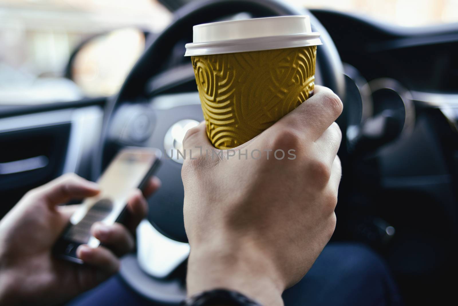 Man arms hold a coffee and rudder in automobile