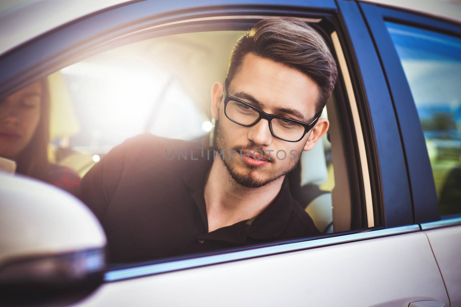 Enjoying travel. Beautiful young couple sitting on the front passenger seats and smiling while handsome man driving a car and use a mobile phone