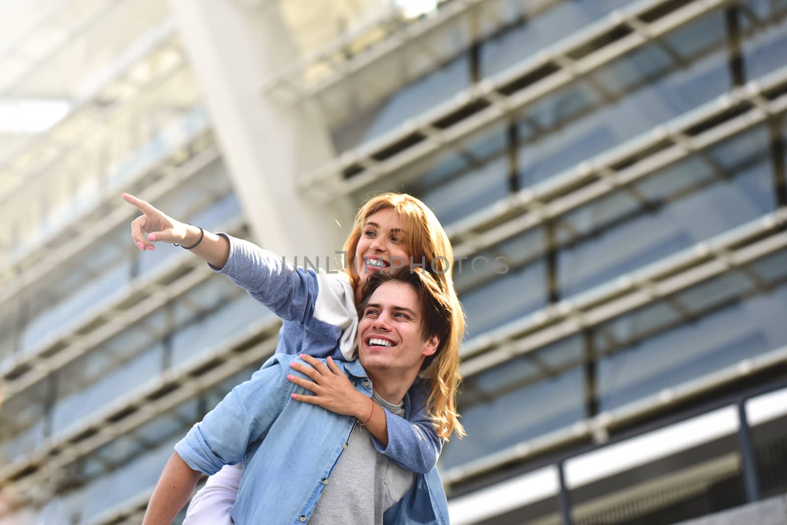 Man giving his pretty girlfriend a piggy back at street smiling at each other on a sunny day.