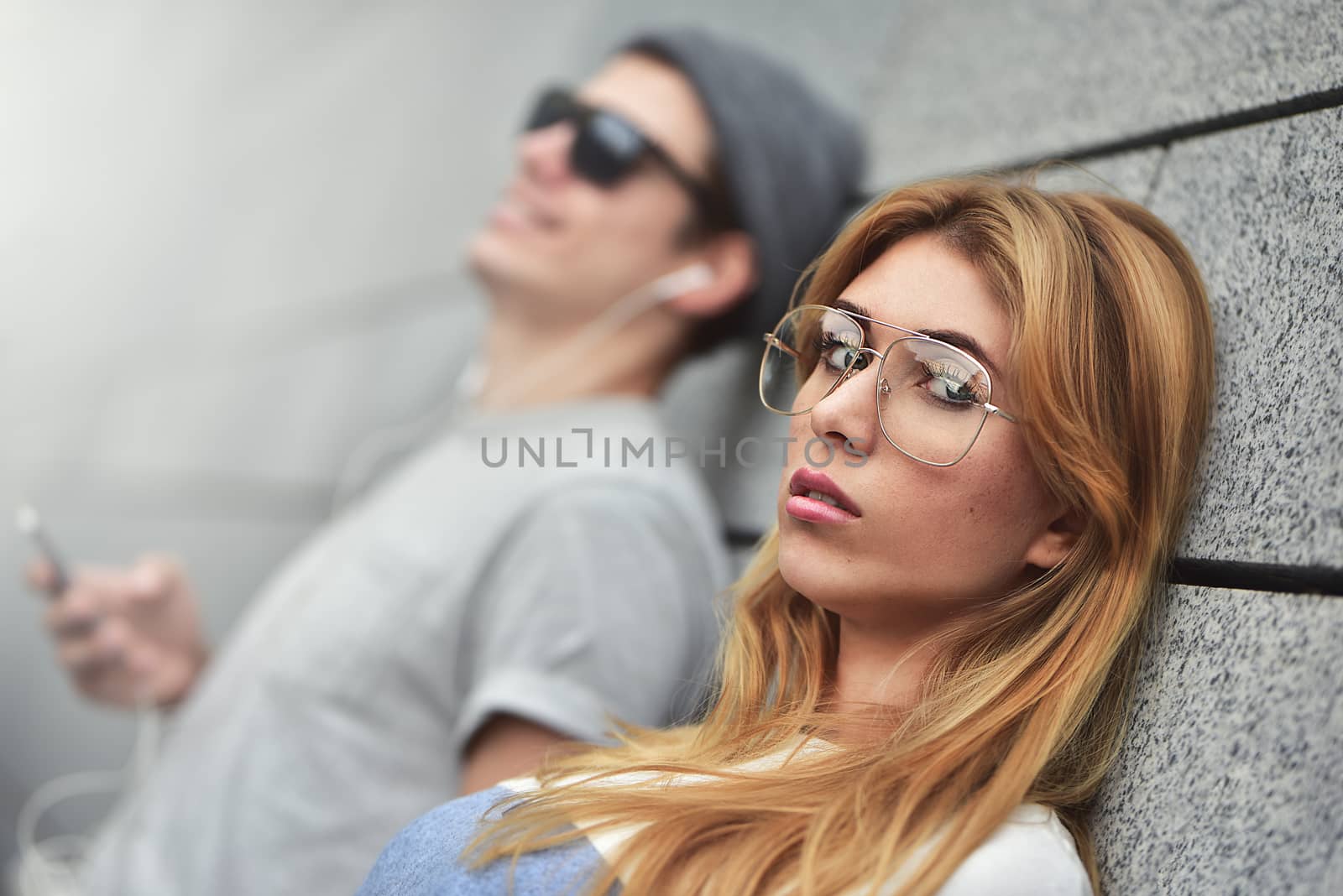 Portrait of Young attractive couple listening to music on the same pair of headphones, dressed in stylish clothes against a background of a gray wall.