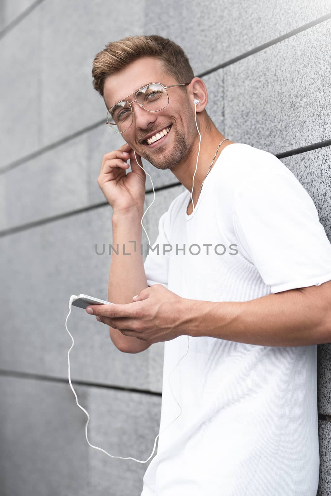 Earphones concept. People, technology, travel and tourism - man with earphones, smartphone on city street and listening to music over gray wall background