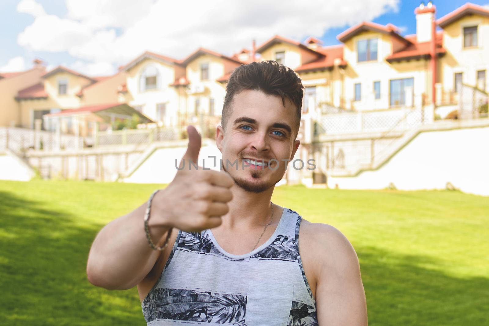 Attractive resting man with thumb up. beautiful cottages in the background