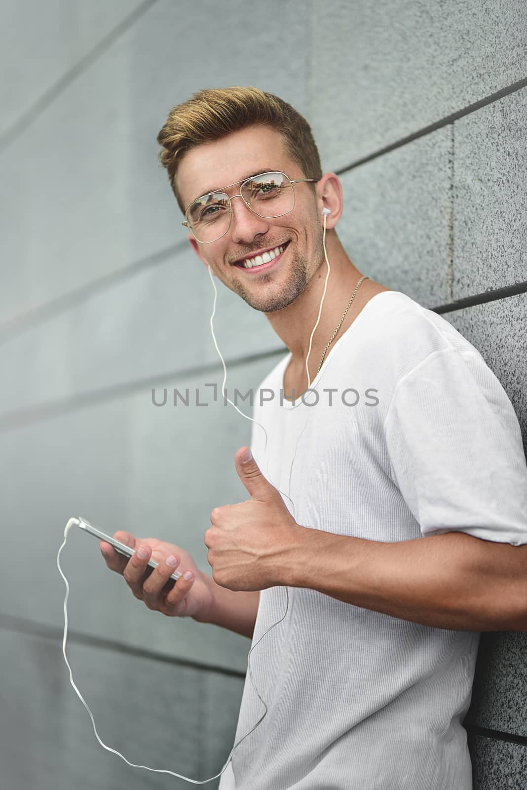 People, technology, travel and tourism - man with earphones, smartphone on city street and listening to music over gray wall background