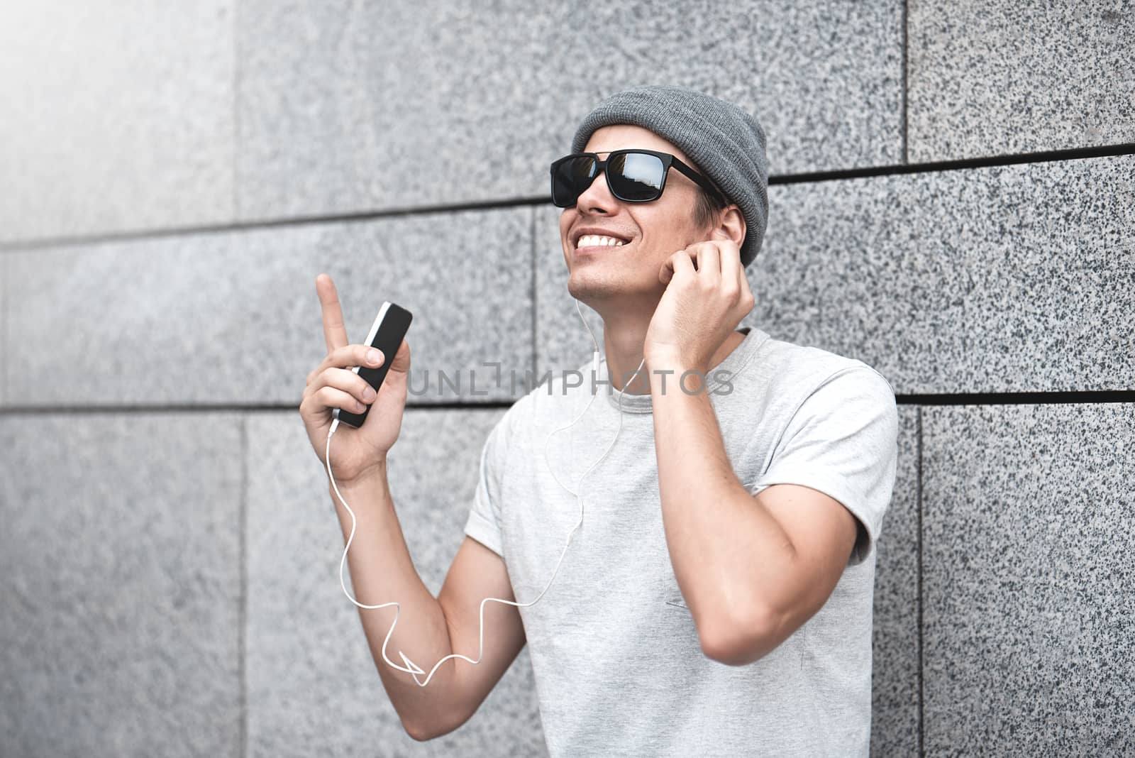 People, technology, travel and tourism - man with earphones, smartphone on city street and listening to music over gray wall background