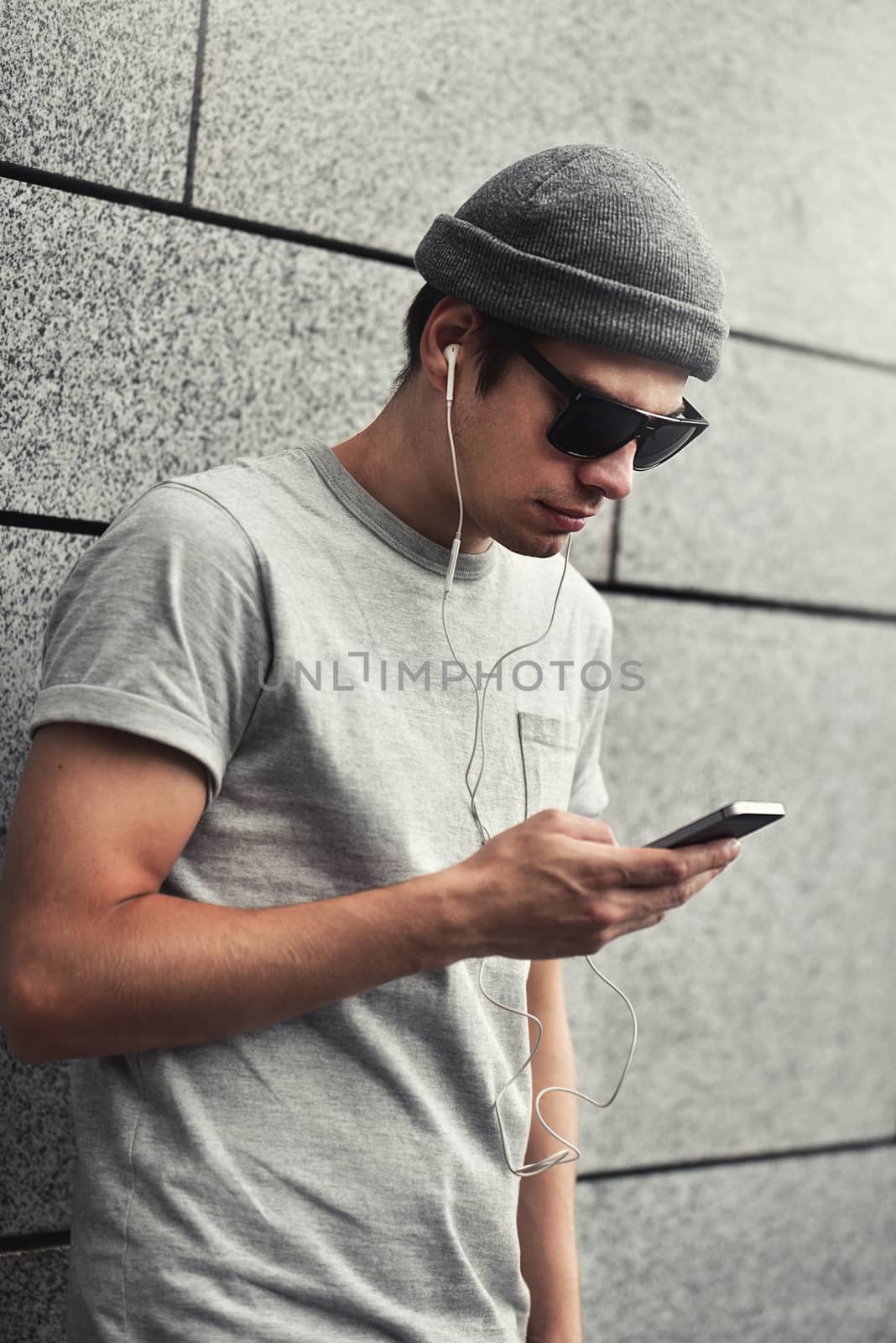 People, technology, travel and tourism - man with earphones, smartphone on city street and listening to music over gray wall background