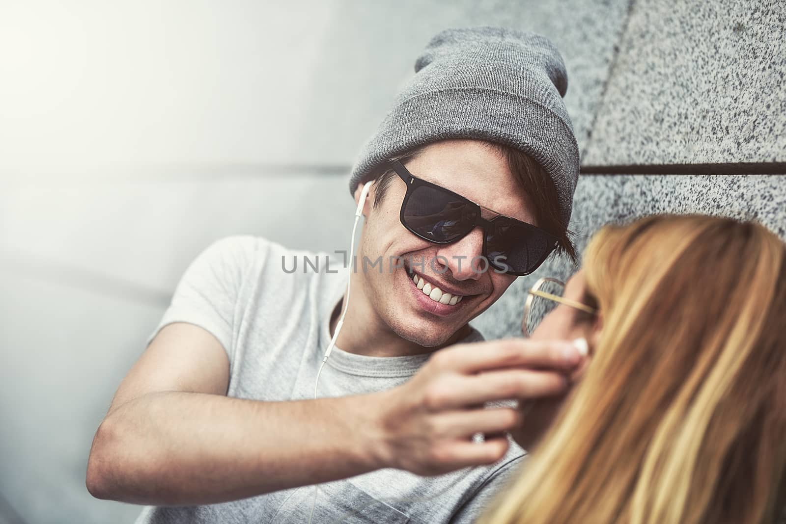 Portrait of Young attractive couple listening to music on the same pair of headphones, dressed in stylish clothes against a background of a gray wall.