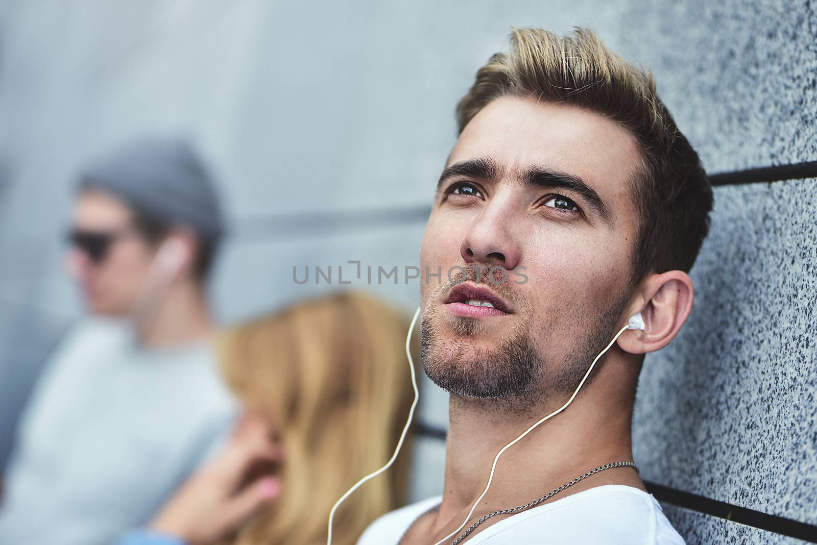 Portrait of Young attractive Teens listening to music on the same pair of headphones, dressed in stylish clothes against a background of a gray wall.