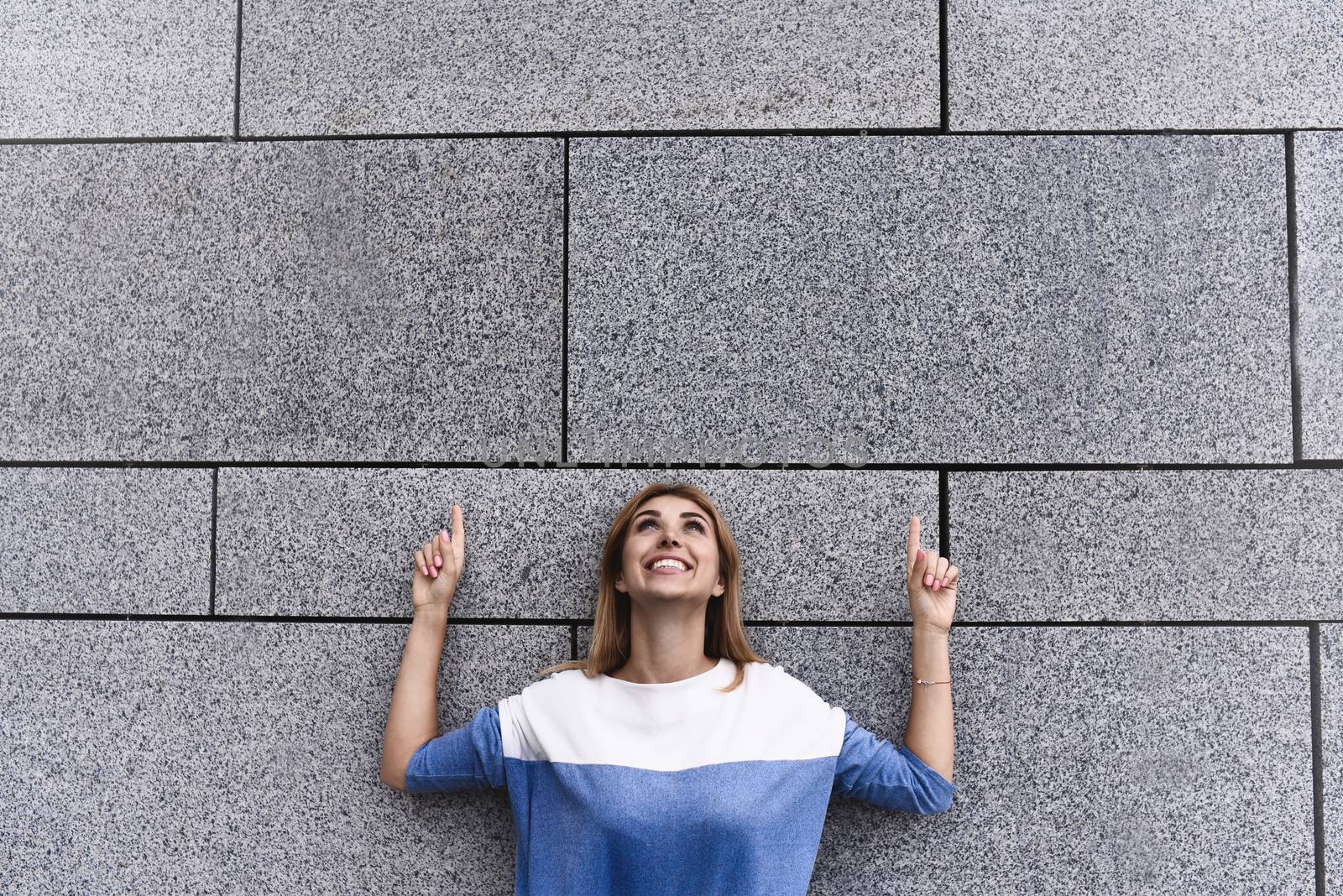Cheerful girl at the street, show a big sale, or nice offer. Advertise concept. People, travel and tourism - woman on city street and girl show with her fingers something over gray wall background