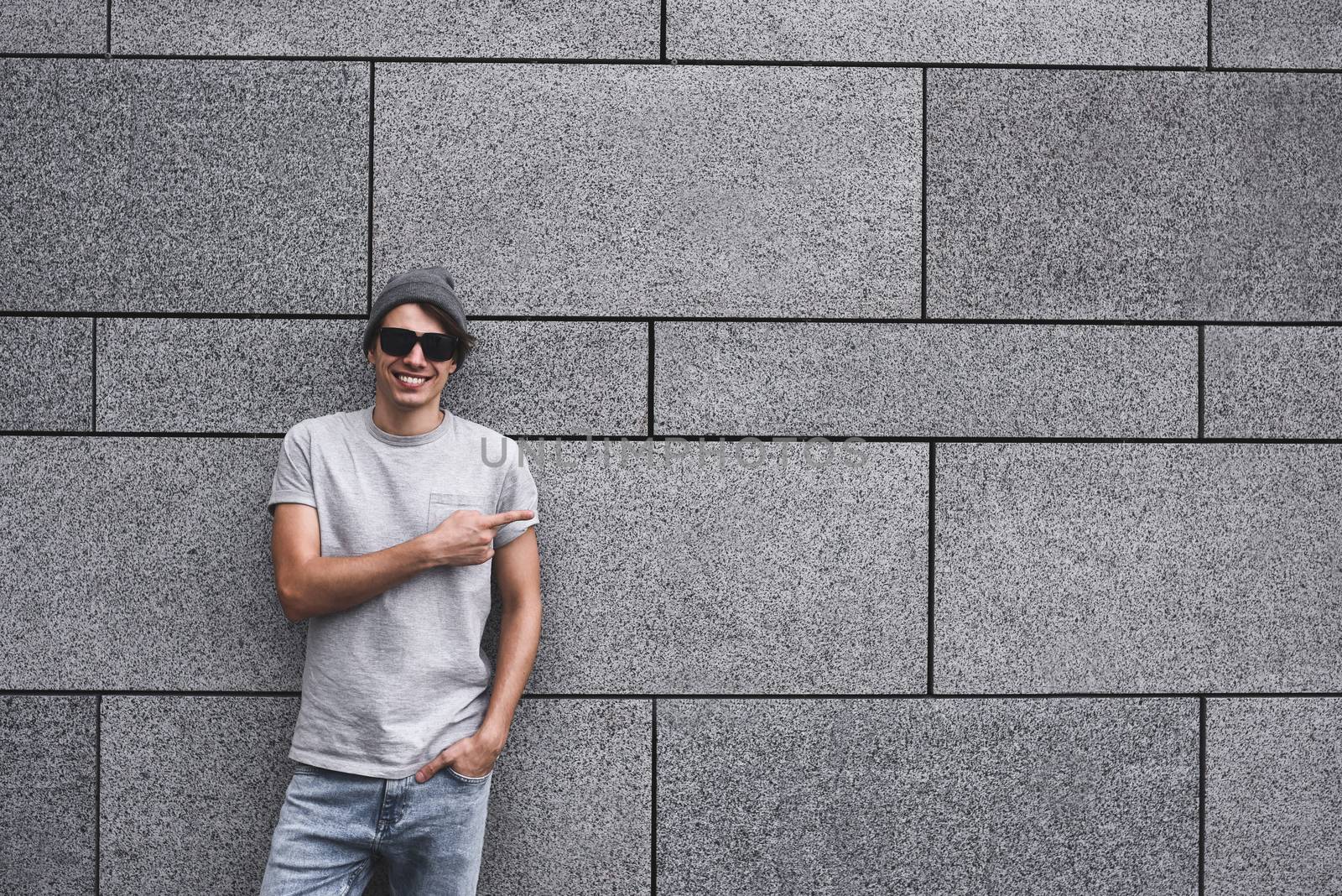 People, travel and tourism - man with Sunglasses on city street and guy show with his finger something over gray wall background
