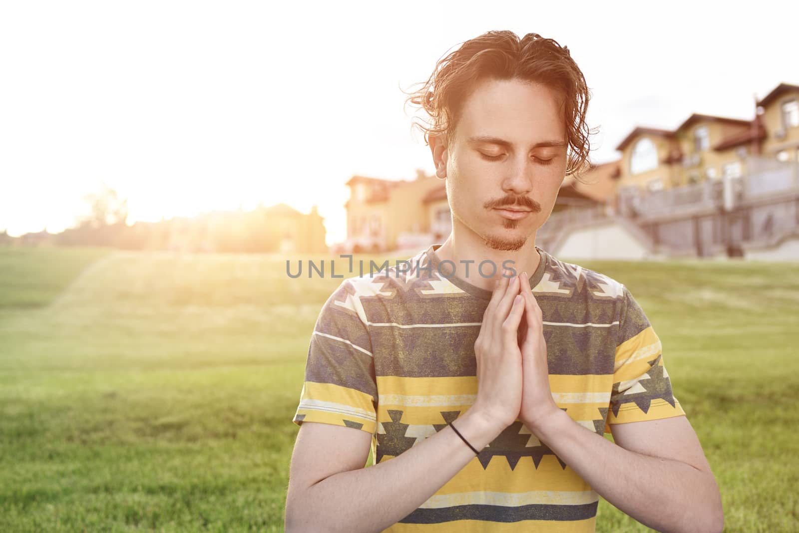 Young man meditating outdoors in the park, sitting with eyes closed and his hands together. man praying to god