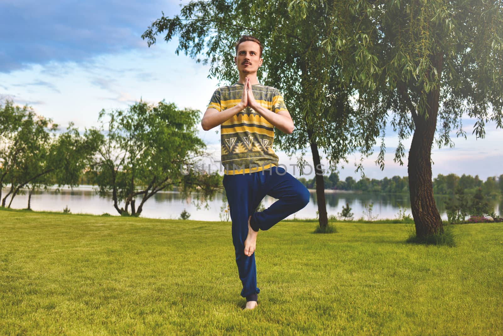 Fitness man doing exercise on one leg isolated in the park. enjoying nature, yoga and meditation concept. spiritual practices.