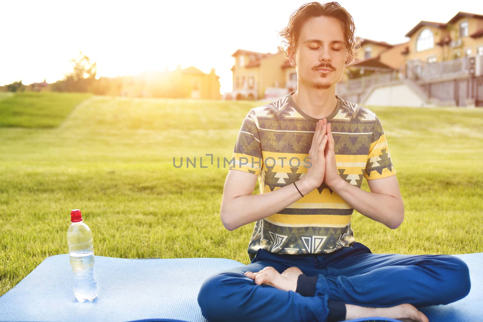 Young man meditating outdoors in the park, sitting with eyes closed and his hands together