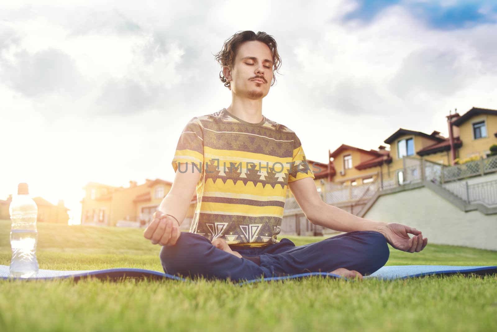 Young man meditating outdoors in the park, sitting with eyes closed and his hands together