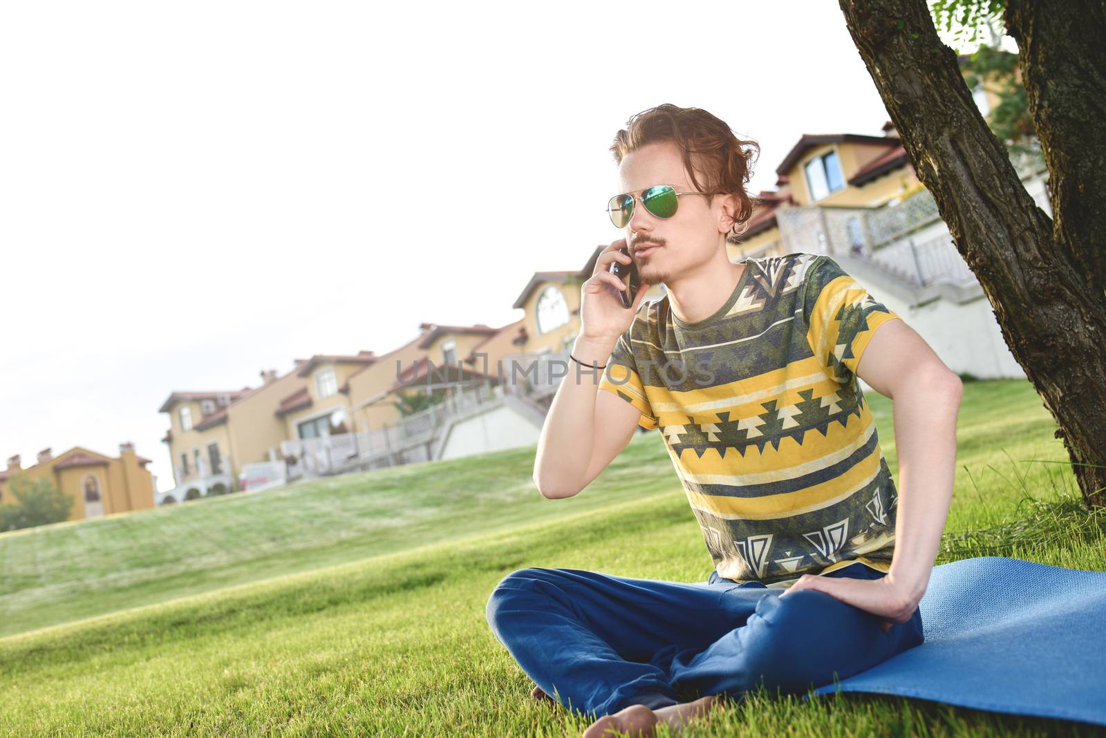 young stylish handsome guy is sitting on grass and talking on the phone resting in the park. Taking a Break