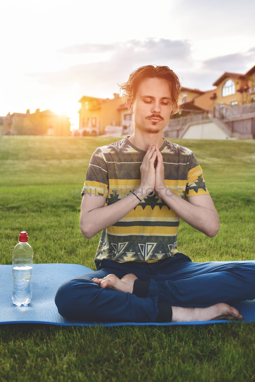 Young man meditating outdoors in the park, sitting with eyes closed and his hands together.enjoying nature, yoga and meditation concept. spiritual practices.zen by Nickstock