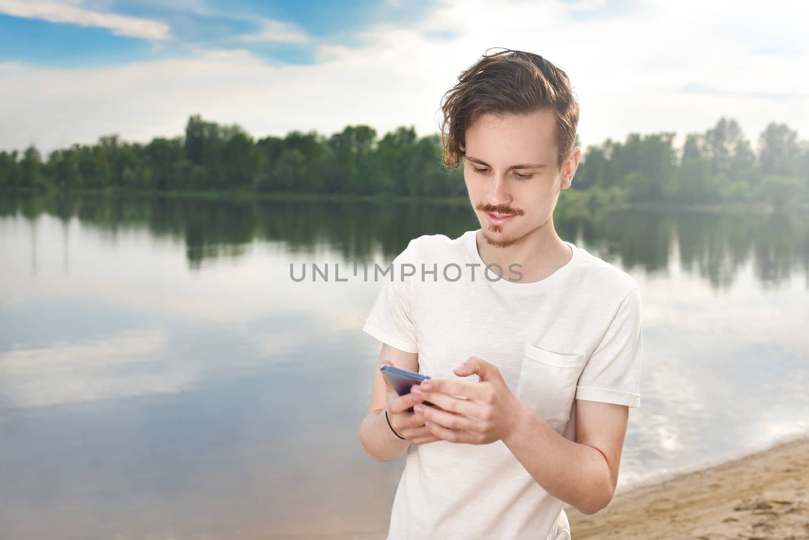 Young man walking near beautiful bay using phone and headphones for communicate with friends . good mood, beautiful view