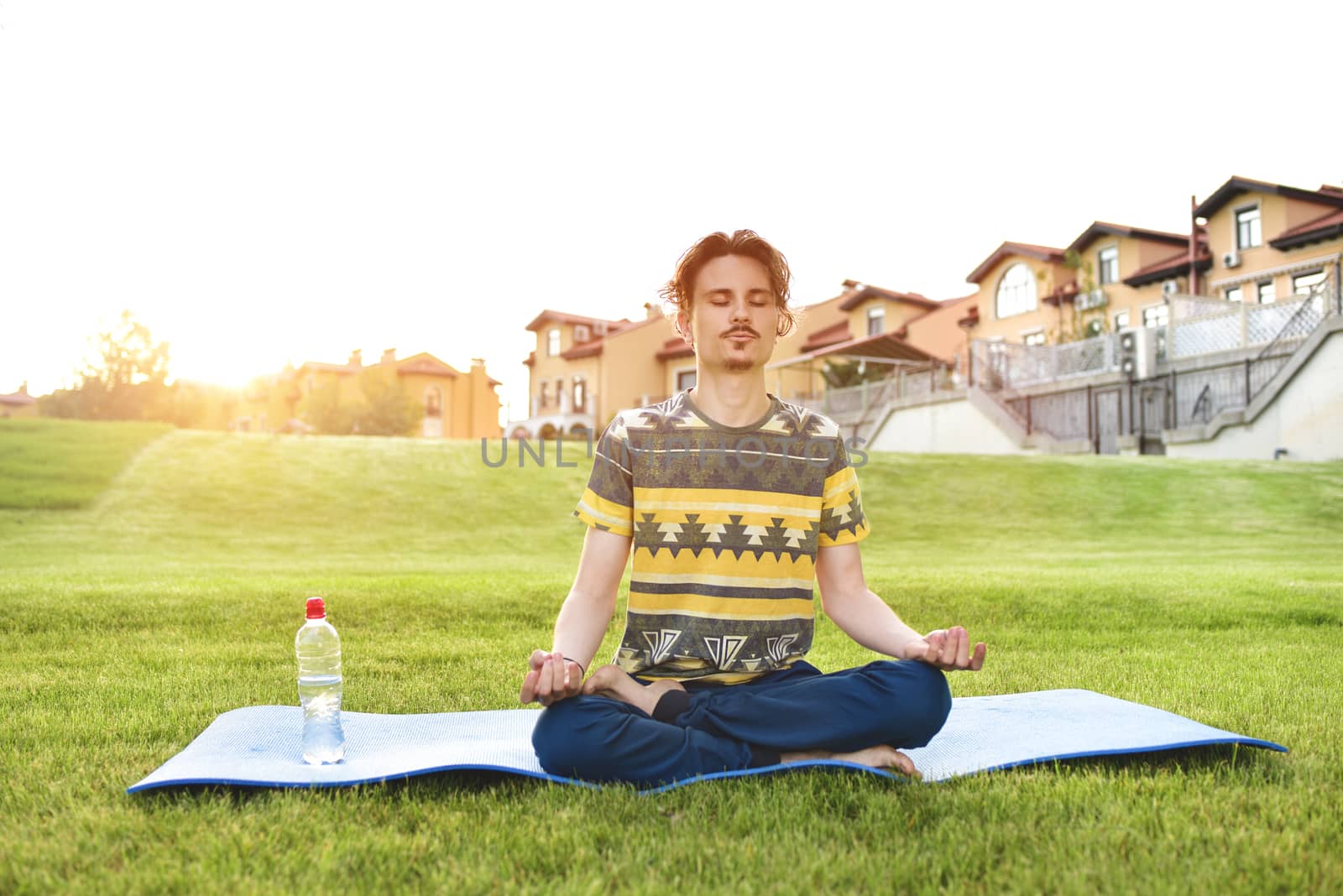 Young man meditating outdoors in the park, sitting with eyes closed and his hands together