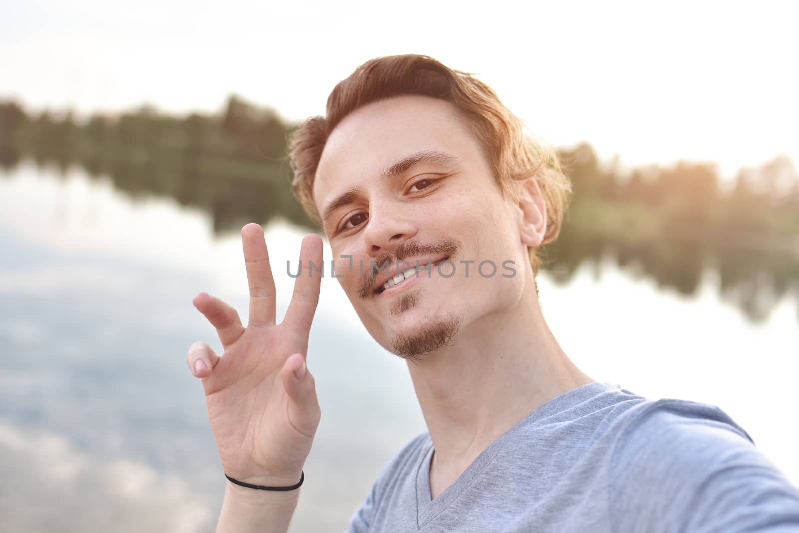 portrait of Young handsome stylish smiling guy makes selfie against the lake. beautiful nature