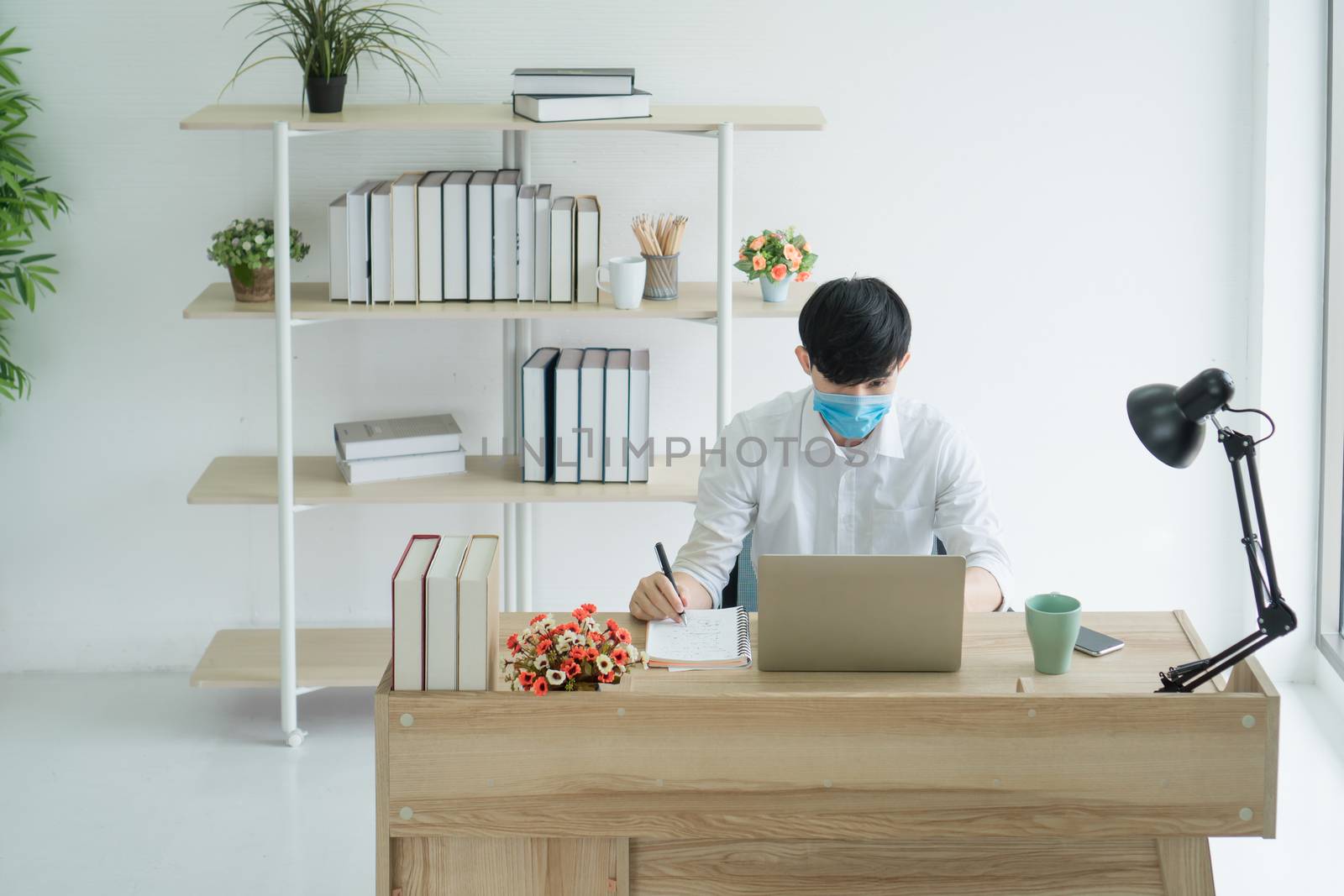 A young Asian man wears a medical mask to work from home. Is a distance from society To prevent the spread of Corona virus