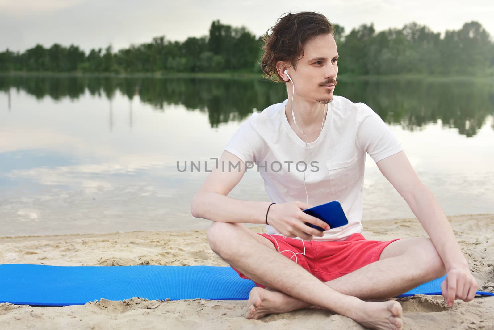 Young man walking near beautiful bay using phone and headphones for communicate with friends and listening music