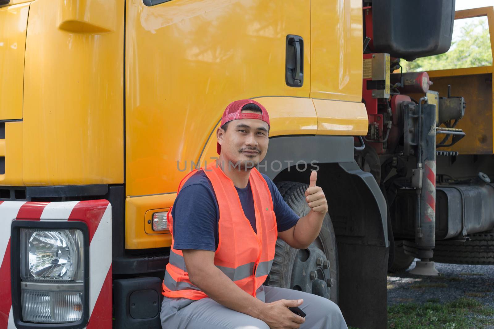 An Asian man was smiling happily at the yellow truck. He has a career as a transport driver. The transportation business never stops. It must be driven and traveled all the time.