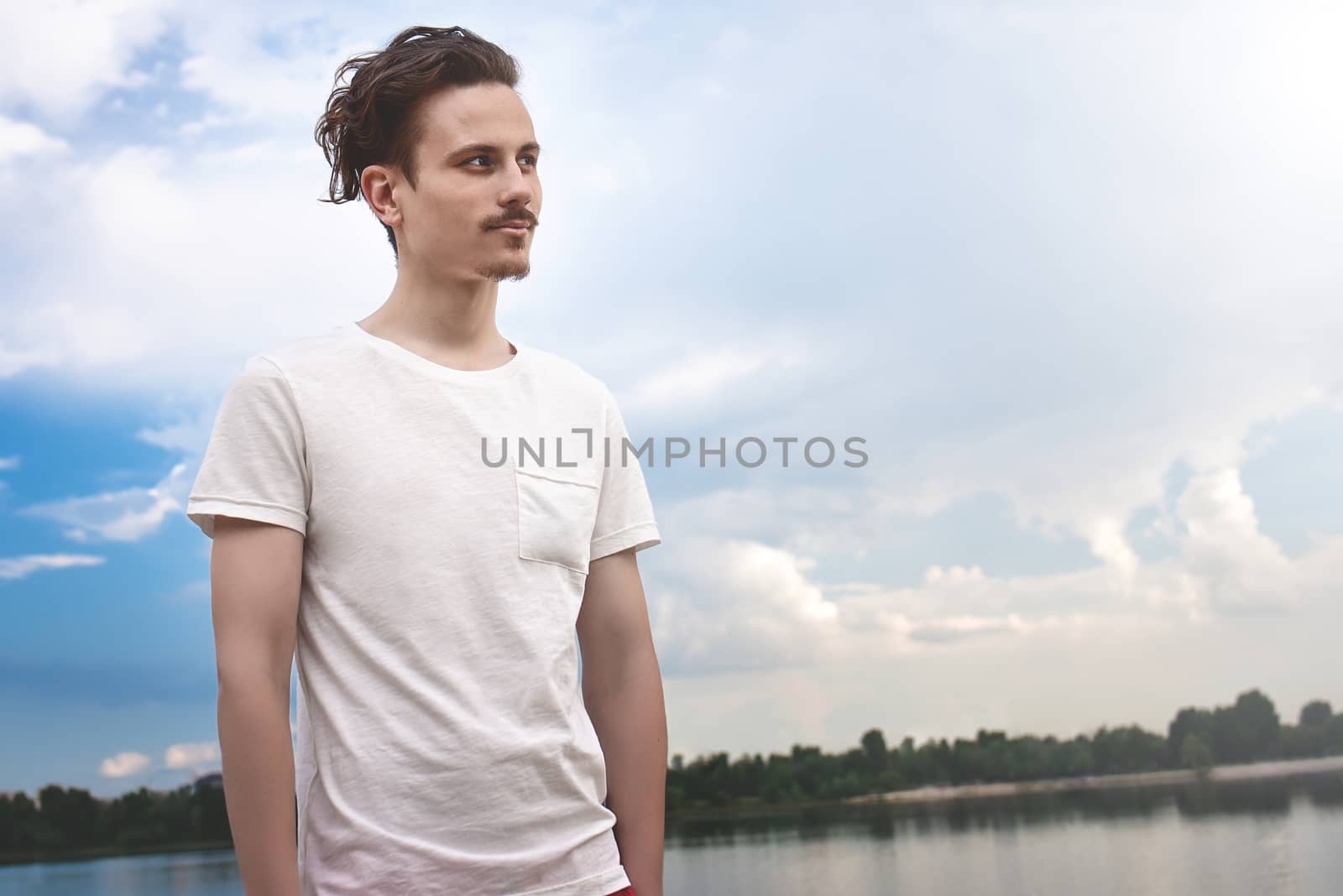 Portrait of Young Man Enjoys a beautiful view and looks into the distance near a lake and forest . summer . spring. nature