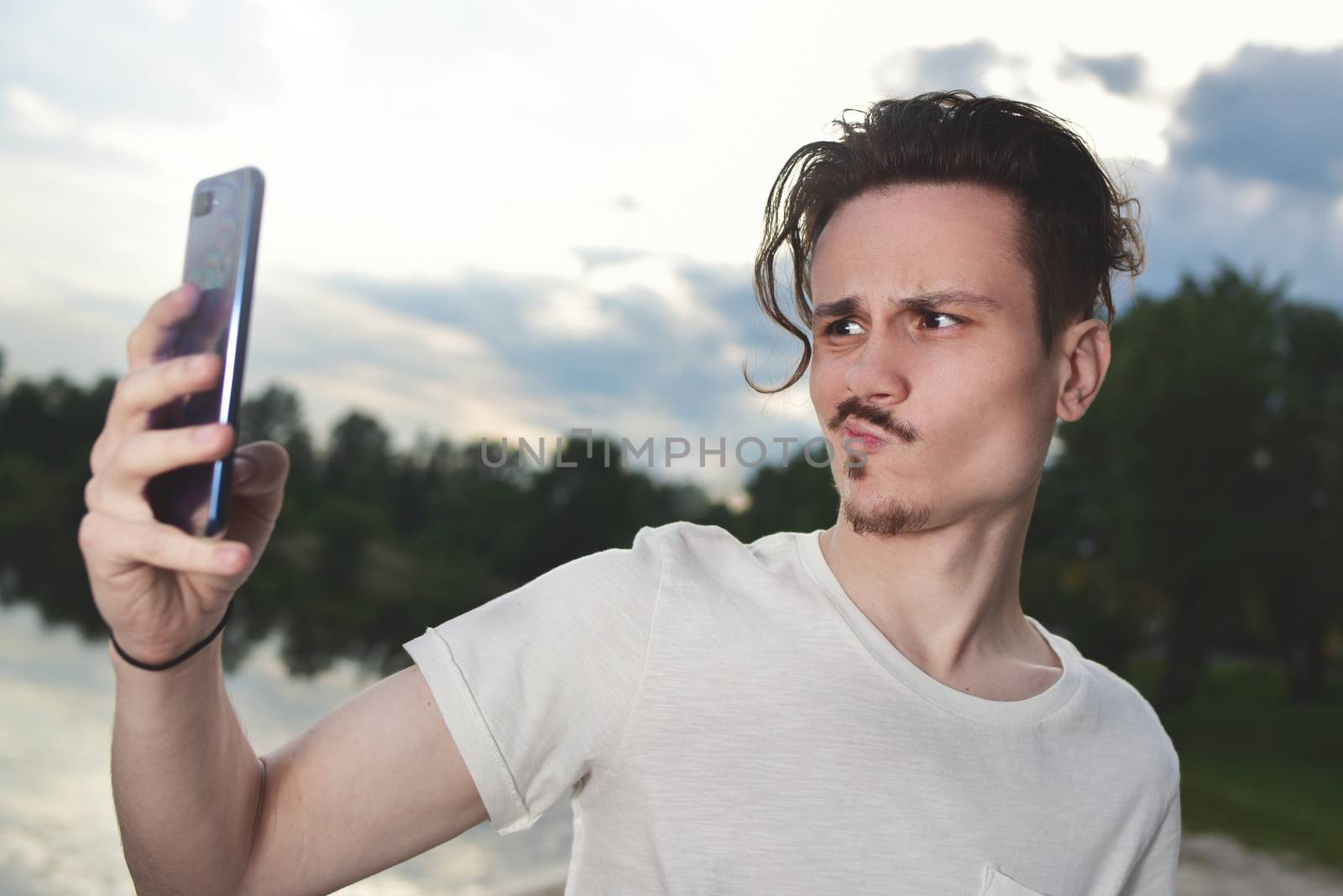the guy grimaces into the camera.frustrated young handsome guy makes unsuccessful selfie on his smartphone in nature,