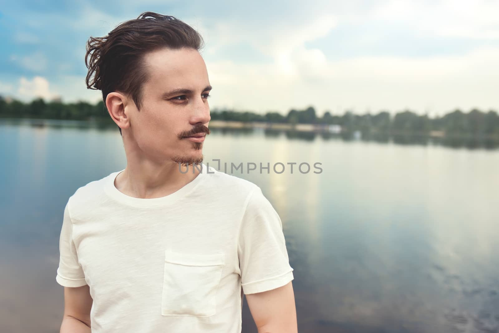 Portrait of Young Man Enjoys a beautiful view and looks into the distance near a lake and forest . summer . spring. nature
