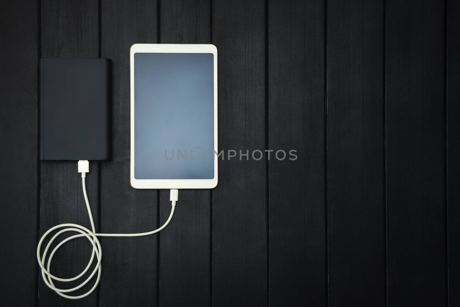 power bank loads tablet PC, smartphone - isolated on wooden background. charging concept. free copyspace