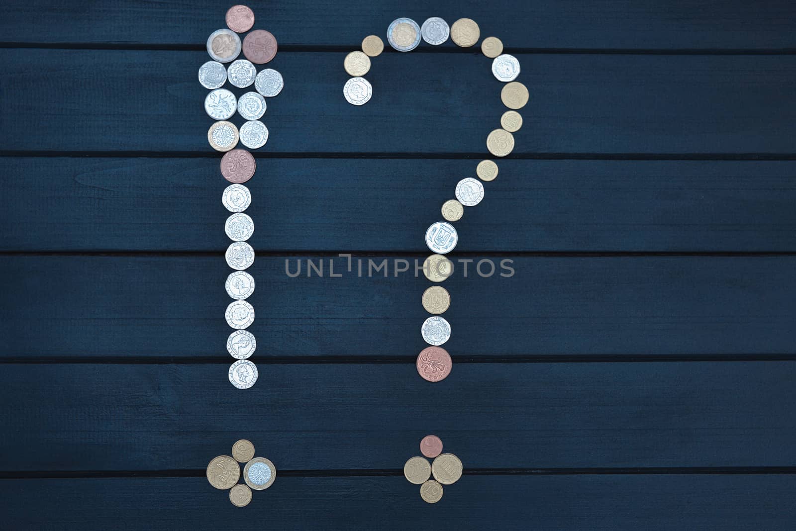 Scattered coins of different countries in the form of a question mark and an exclamation point on wooden table.