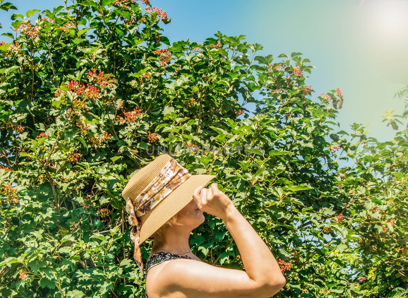 A happy young woman in a romantic hat enjoys the sunshine in a summer Park, looks at the Sunny sky, travel concept, side view, no face.