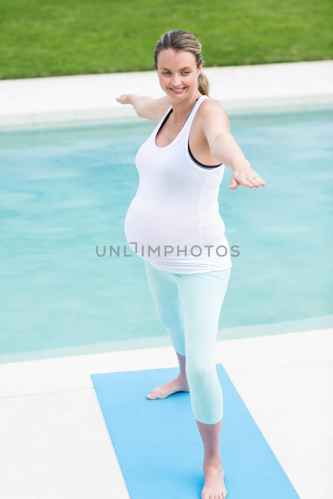Pregnant woman doing yoga next to the swimming pool