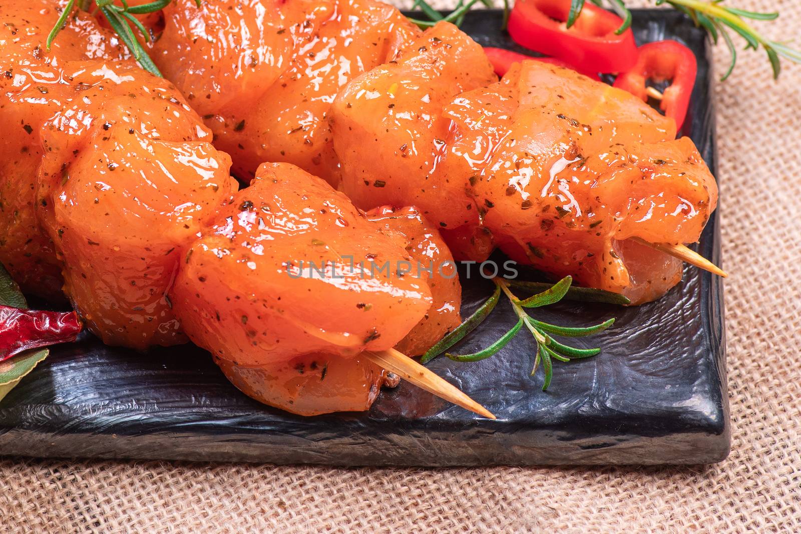 Raw marinated and spicy chicken skewers.Raw chicken skewers in marinade with spices on a black plate and on a wooden table. Top view. Chicken meat close up. Raw meat in marinade. Tasting diet meat. by nkooume