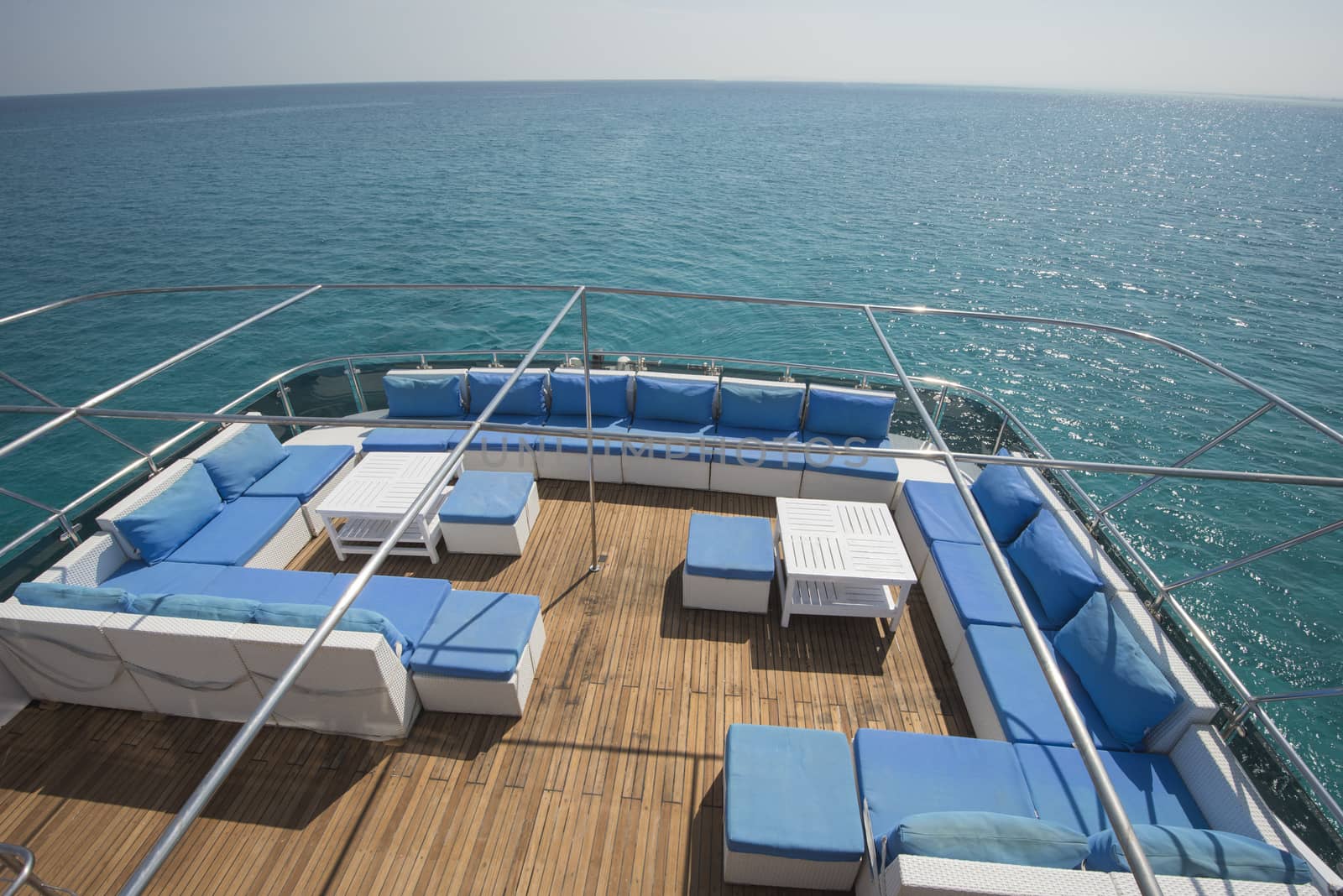 Rear teak deck of a large luxury motor yacht with chairs sofa table and tropical sea view background