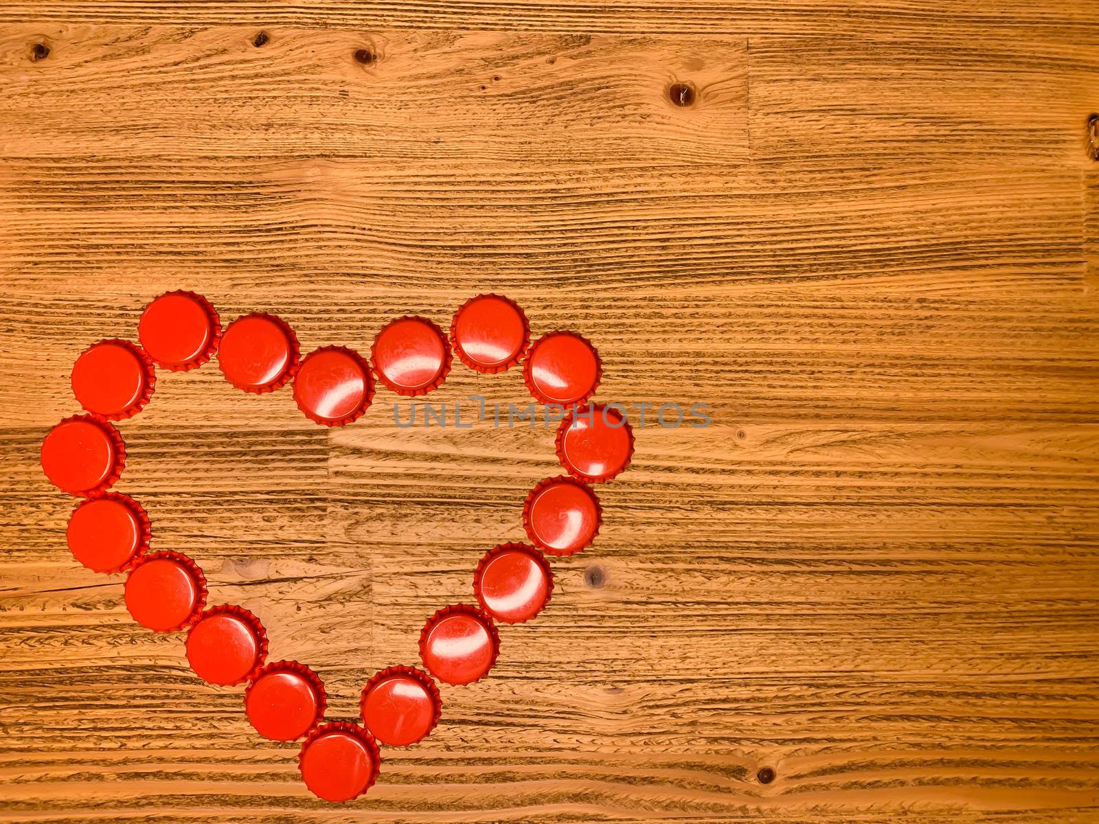 Red love heart made from beer bottle tops lids on a rustic wooden table. Beer drinkers Valentine's day concept, top view horizontal stock image with empty space for text