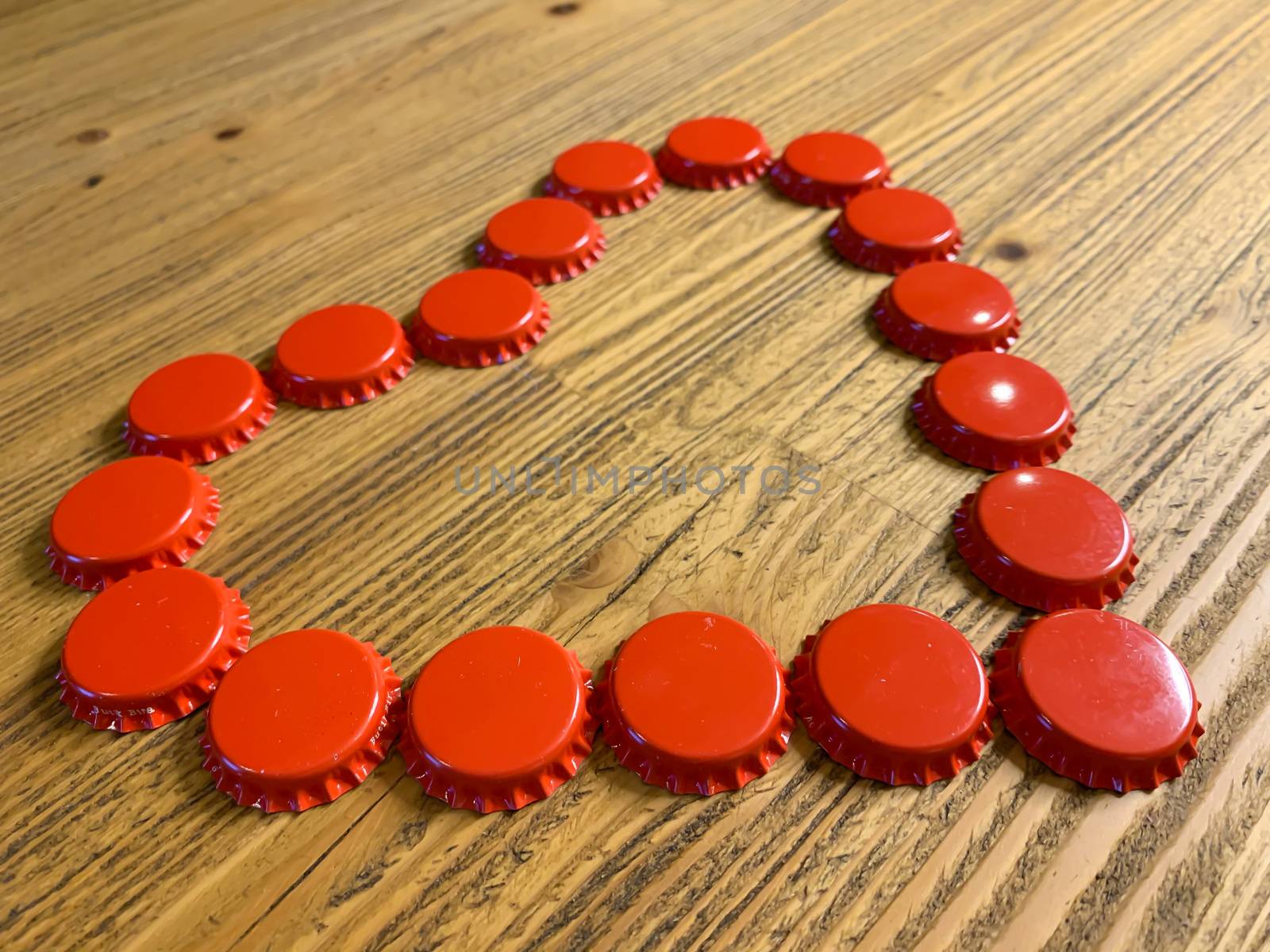 Red love heart made from beer bottle tops lids on a rustic wooden table. Beer drinkers Valentine's day concept, top view horizontal stock image.