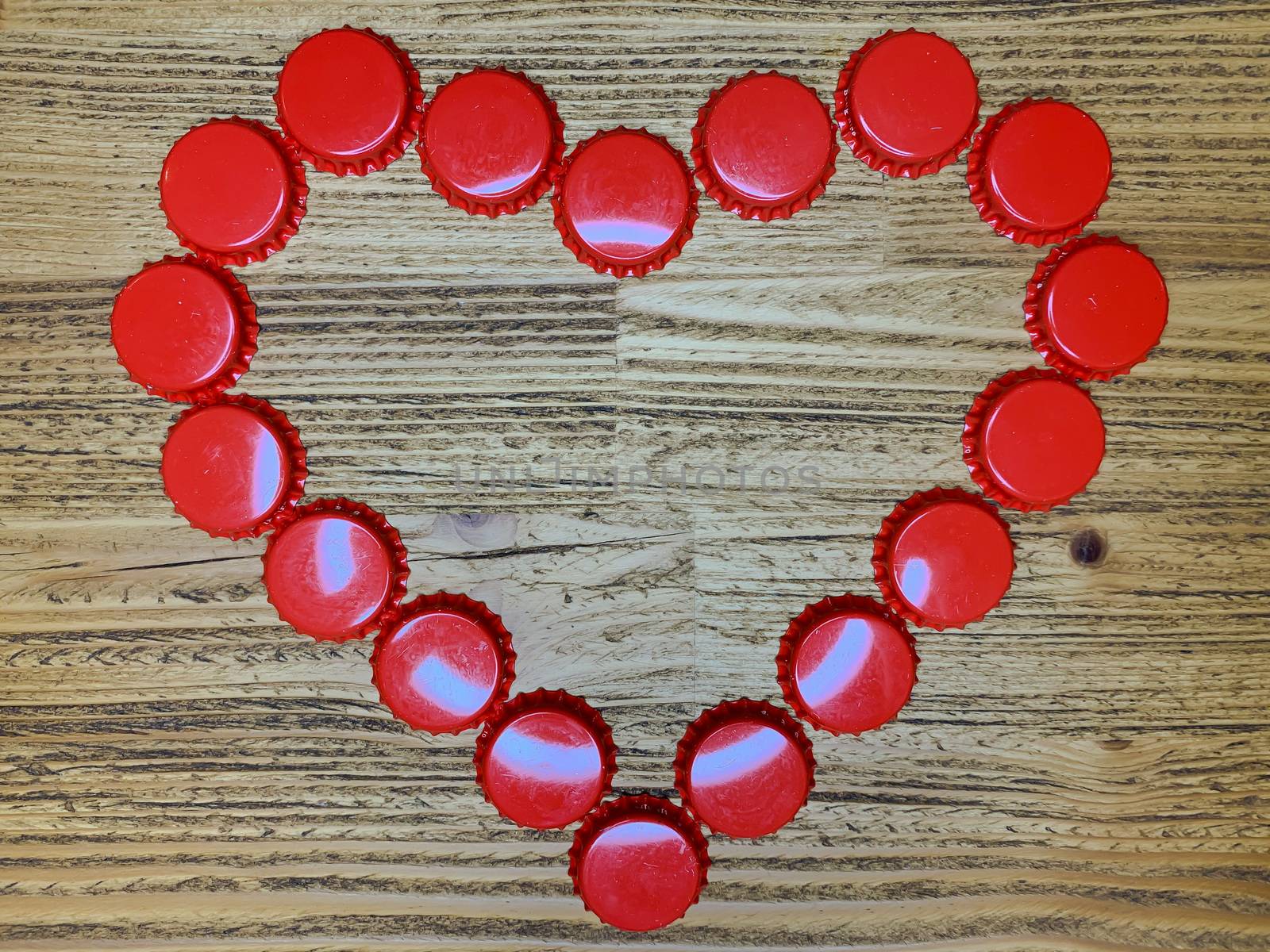 Red love heart made from beer bottle tops lids on a rustic wooden table. Beer drinkers Valentine's day concept, top view horizontal stock image.