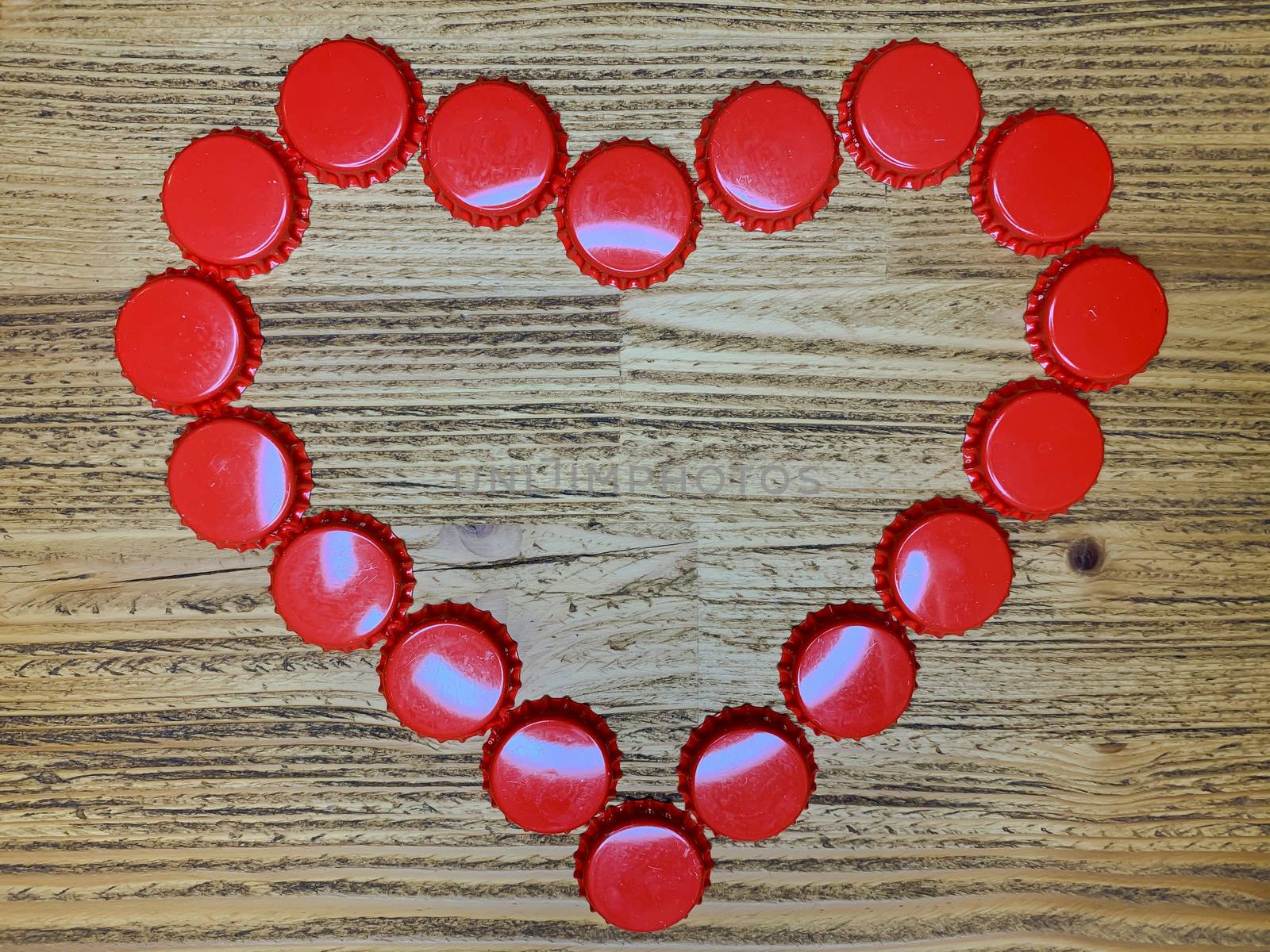 Red love heart made from beer bottle tops lids on a rustic wooden table. Beer drinkers Valentine's day concept, top view horizontal stock image.