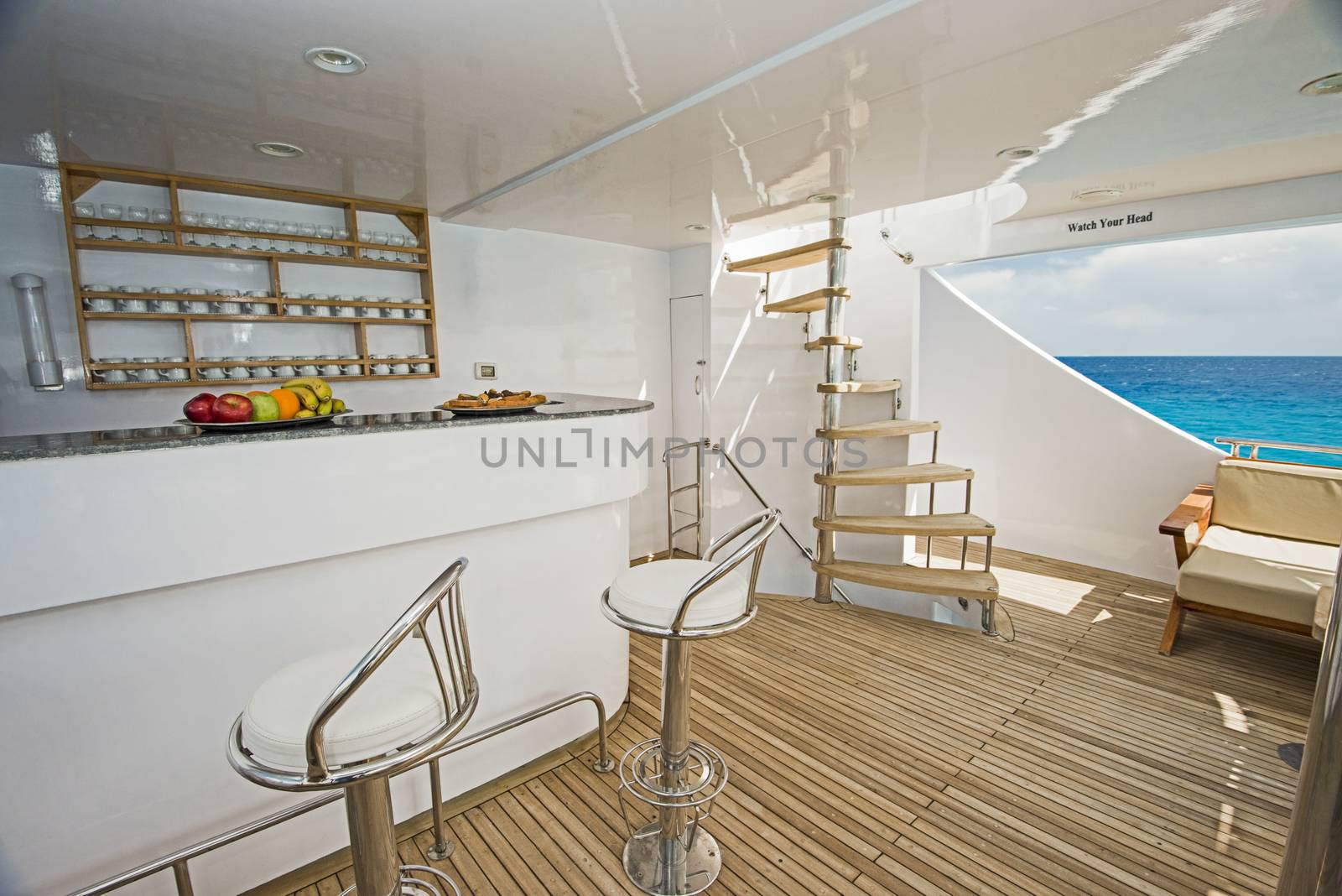 Rear sundeck of a large luxury motor yacht with bar area and tropical sea view background