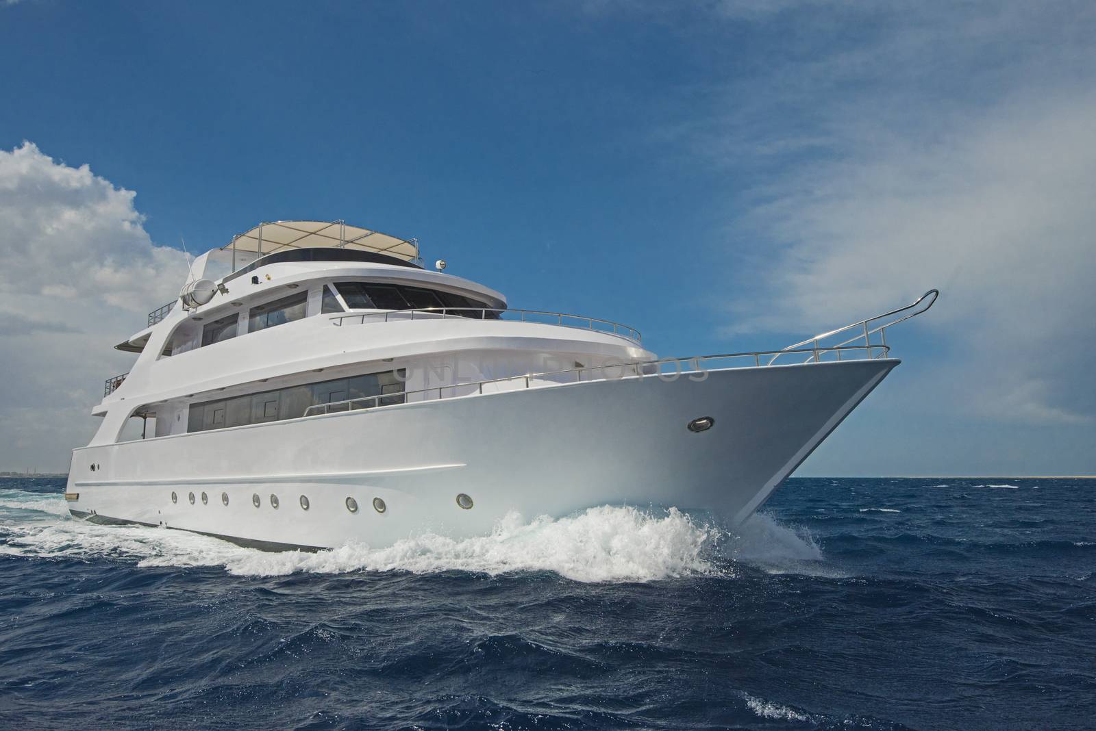 Large luxury motor yacht under way sailing out on tropical sea ocean with cloudy sky background
