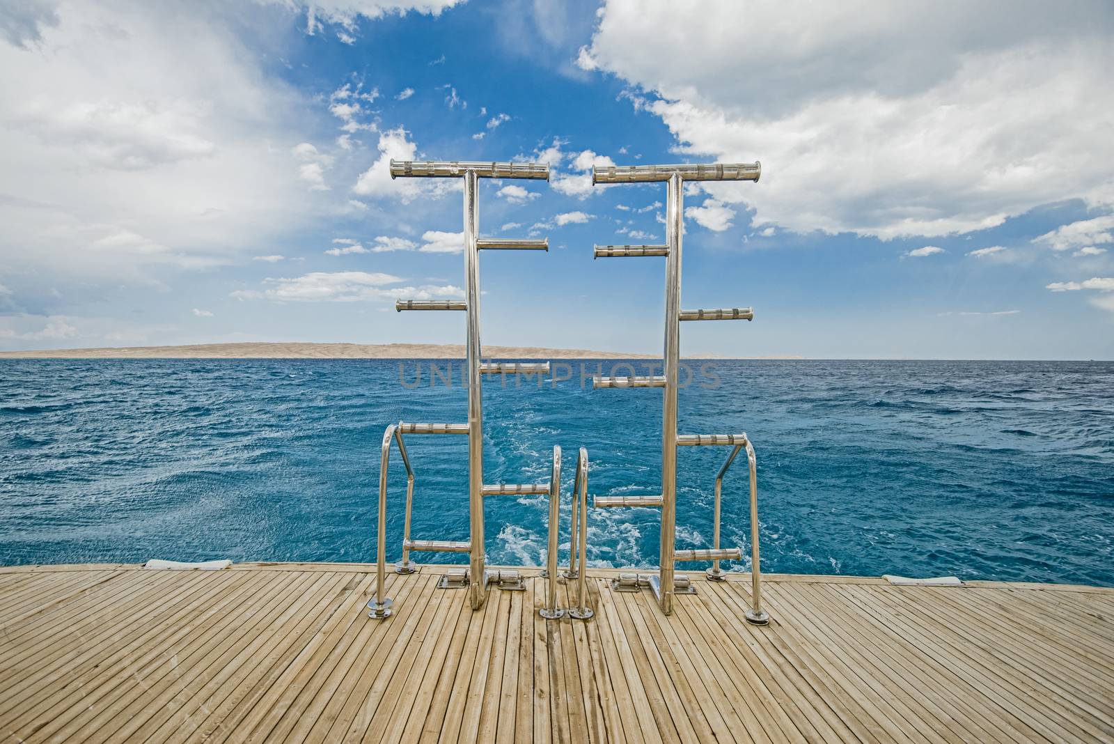 Metal steel ladders on back teak deck of a luxury motor yacht sailing on a tropical ocean with cloudy sky background