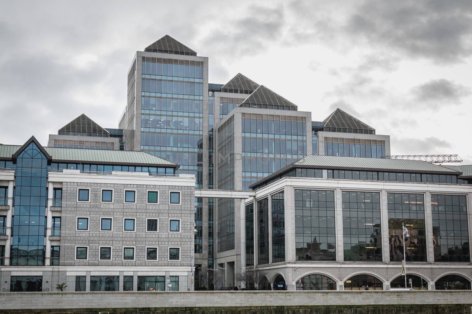 Dublin, Ireland - February 12, 2019: View of the modern building of the Irish commercial bank Ulster Bank next to the River Liffey where people walk on a winter day